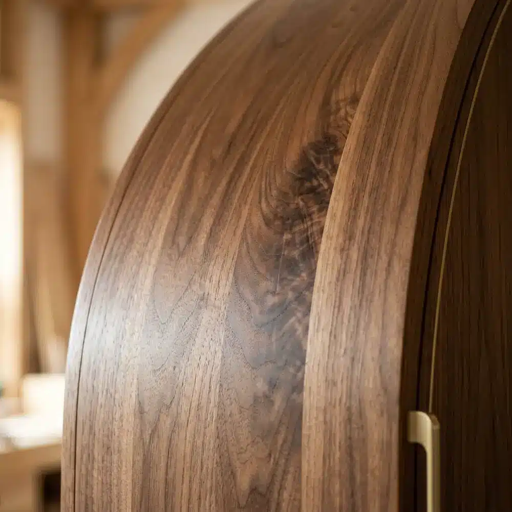 Gros plan sur un placage en noyer naturel épousant la forme courbée d'une façade de meuble sur mesure.